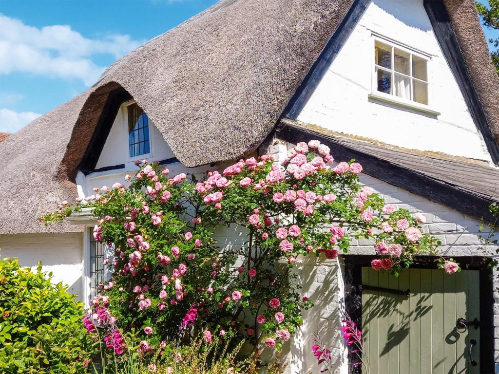 新米尔顿Smugglers Cottage的茅草小屋,门上摆放着粉红色的鲜花