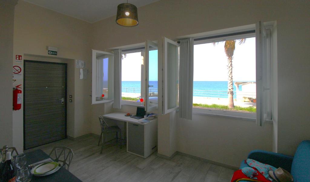卡普多兰多Capo d'Orlando Apartments - Doria 52的客厅配有书桌和2扇窗户,享有海滩美景。