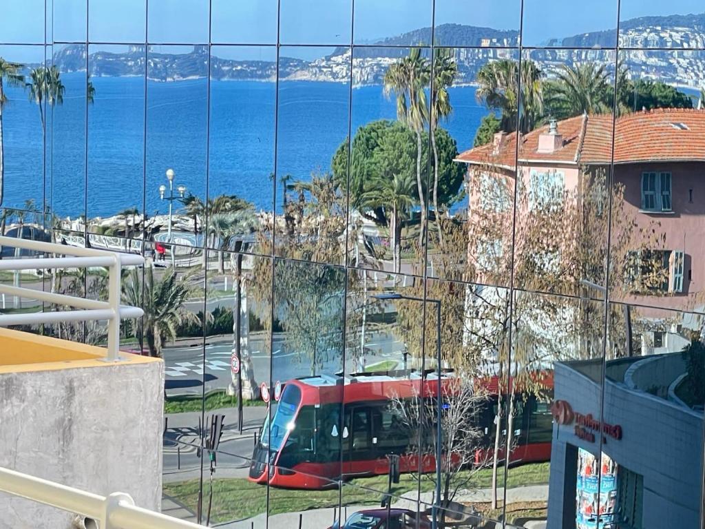 尼斯STUDIO SUR LA PROMENADE DES ANGLAIS AVEC VUE MER ORIGINALE À 40 m DE LA PLAGE的沿着海边的街道行驶的红色巴士