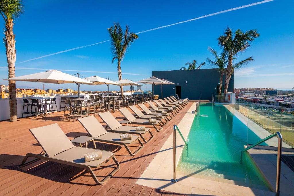 马拉加Hotel Málaga Vibes的游泳池旁的一排椅子和遮阳伞