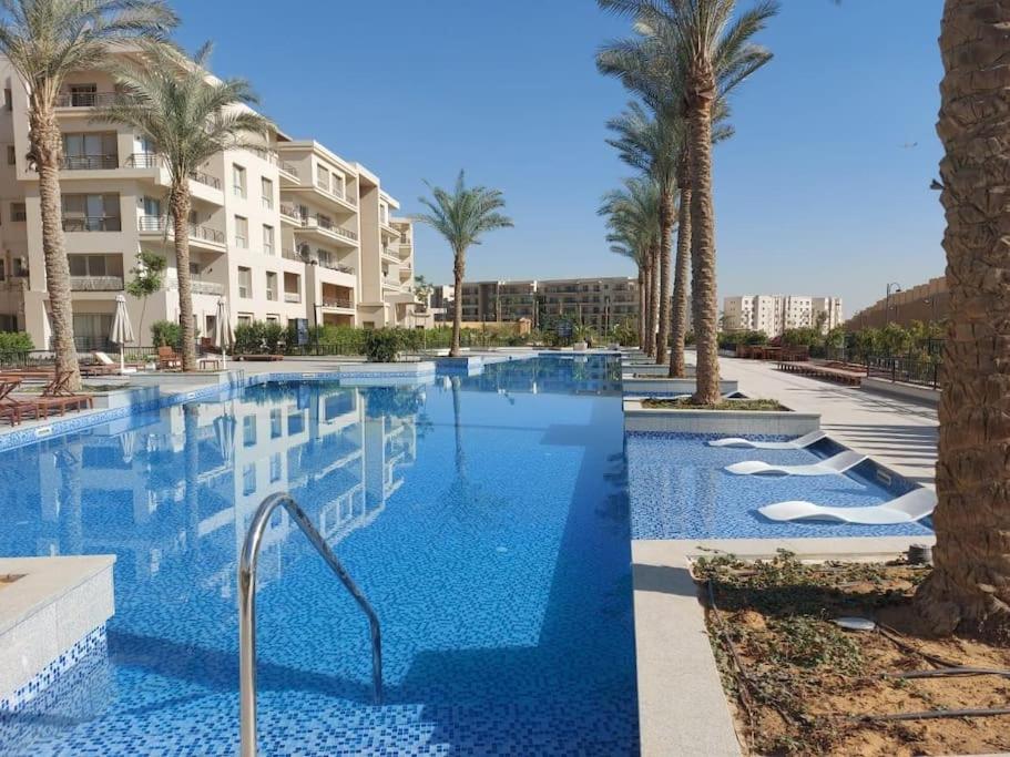 开罗Alumia Marigold Suite 3BR Apt Pool Access的一座棕榈树游泳池和一座建筑