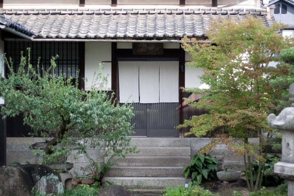 日々の宿: 宇野駅から車で5分 直島へ 最大7名様 古民家貸切 一棟貸し的一座有白色门和一些树木的房子