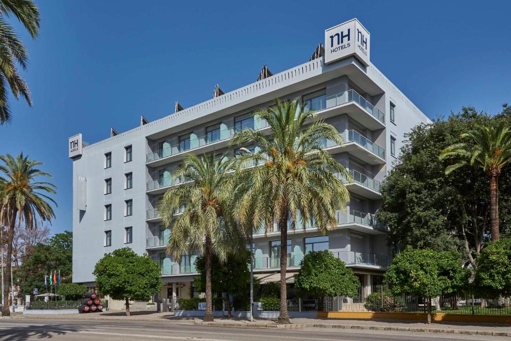赫雷斯-德拉弗龙特拉NH阿维尼达赫雷斯酒店的一座白色的建筑,前面有棕榈树