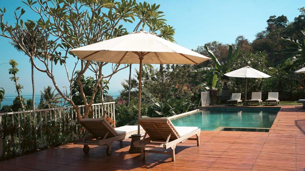 蓝梦岛La Gautch Bungalow的一个带两把椅子和一把遮阳伞的庭院,毗邻一个游泳池