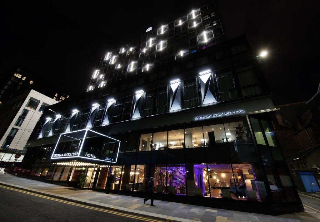 格拉斯哥Sandman Signature Glasgow Hotel的一座建筑,在晚上有人在建筑前面行走