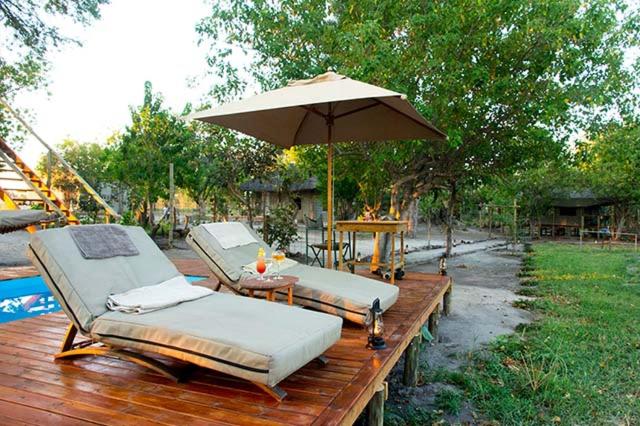 KhwaiCandies Vacation Cottage Khwai的木甲板上的两张床,配有遮阳伞