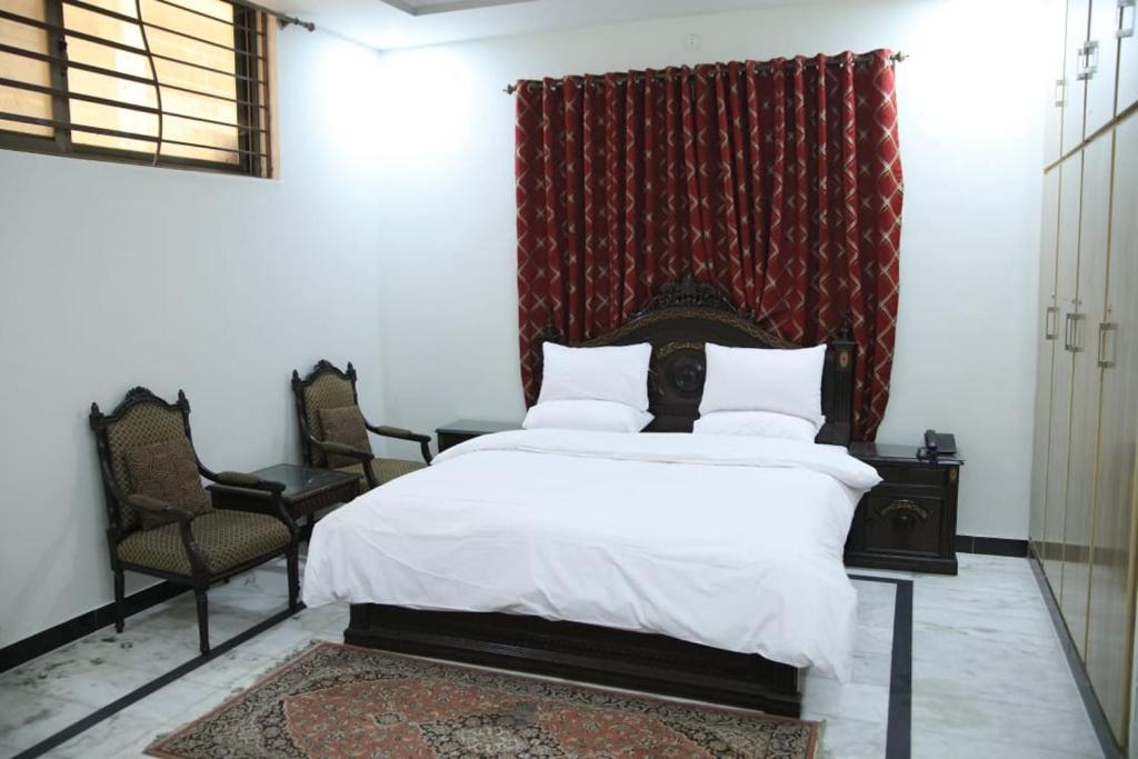 卡拉奇Pramier Inn Near Agha Khan Hospital的卧室配有白色的床和2把椅子
