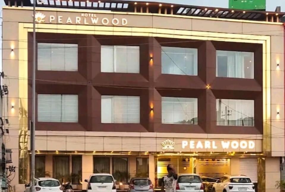 齐拉克普尔HOTEL PEARL WOOD (A unit of olive hospitality group)的一座大型建筑,前面有汽车停放