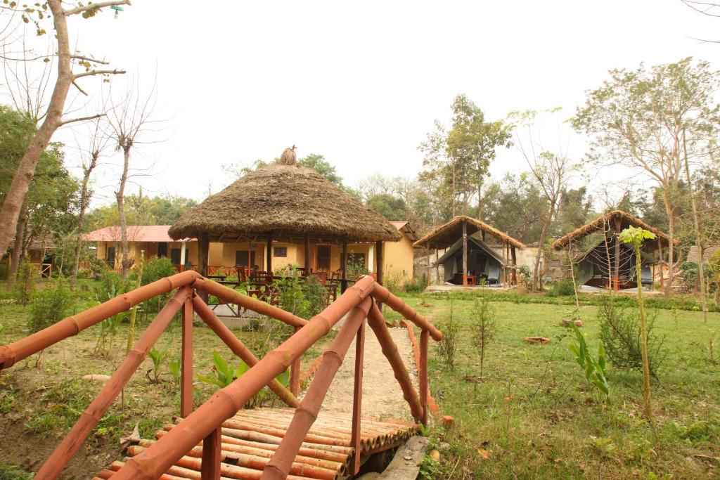 BhurkīāForest Hideaway Resort Pvt Ltd的茅草屋顶的房子和前面的桥梁