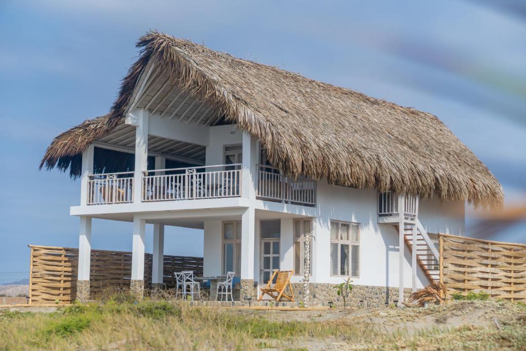 曼克拉Casa Azul Departamentos frente al mar的海滩上带茅草屋顶的房子
