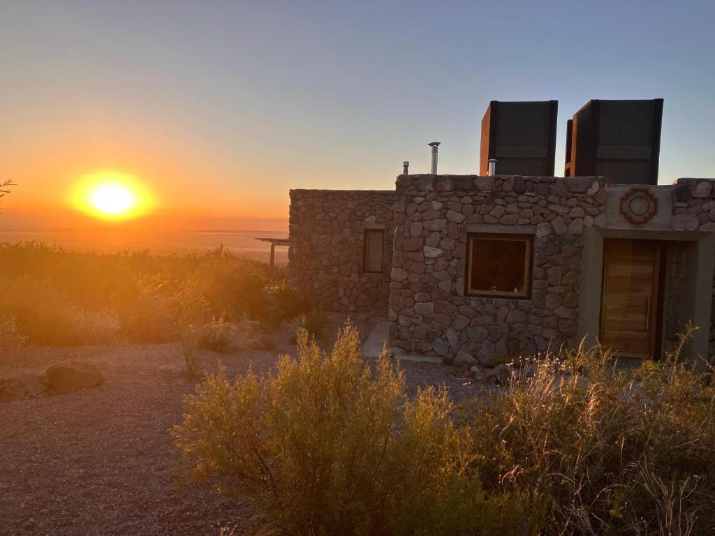 卢汉德库约Bendita Piedra Suites, Las Compuertas Lujan de Cuyo的一座石头房子,背景是日落