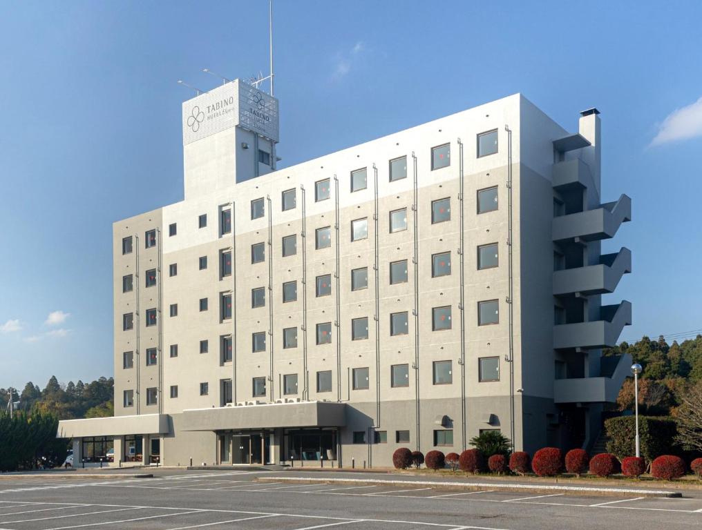 成田Tabino Hotel EXpress Narita的一座白色的大建筑,前面设有停车场