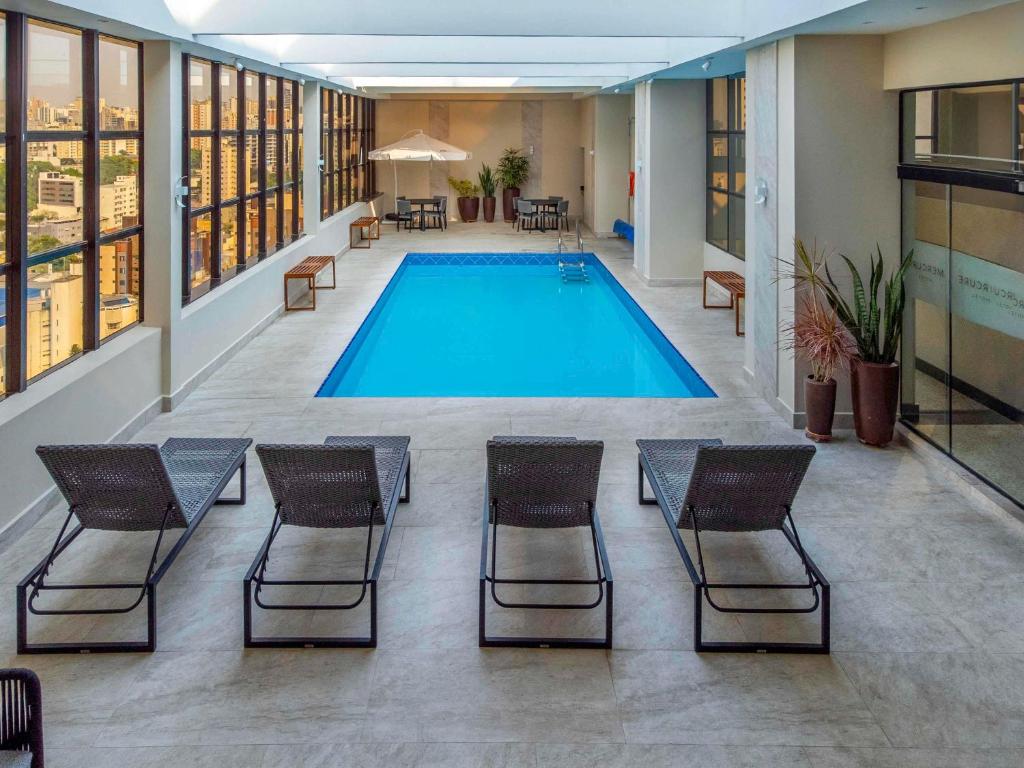 库里提巴库里提巴金色美居酒店 的一座带椅子的建筑中的游泳池以及一座游泳池