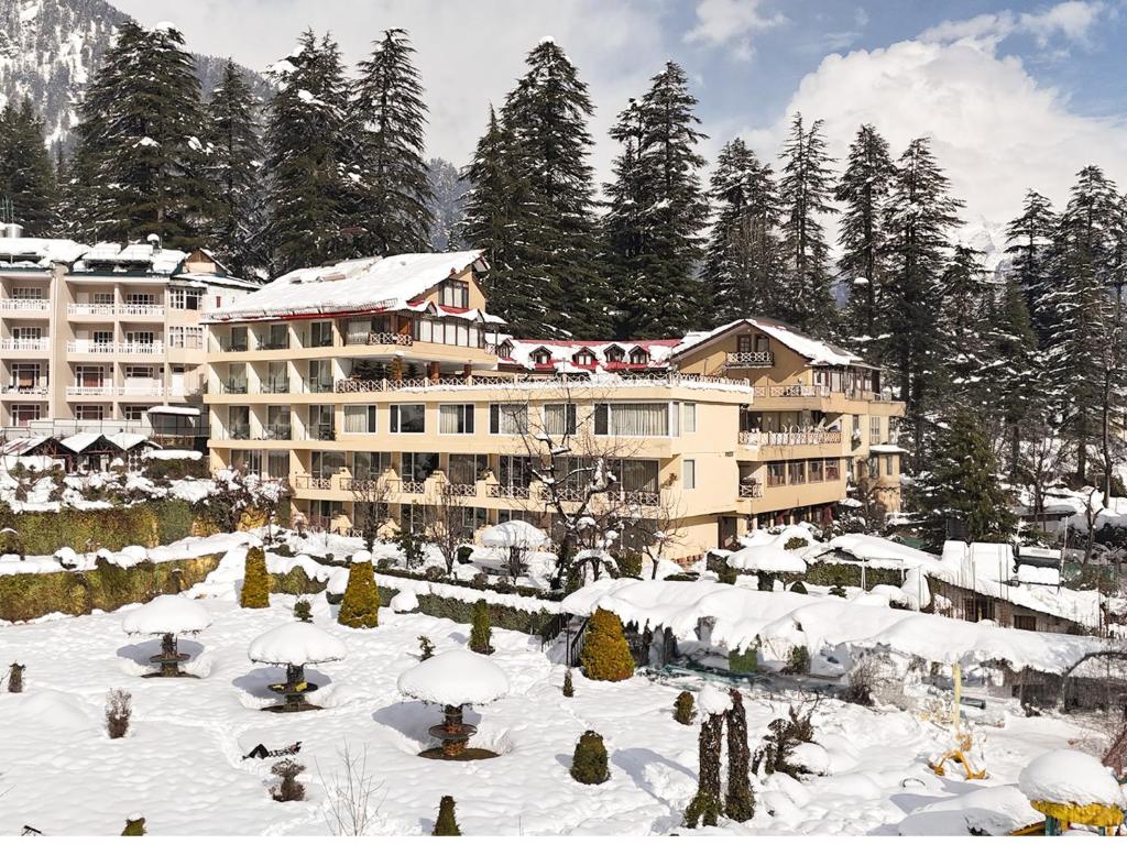 马拉里Snow Valley Resorts & Spa Manali的一座大建筑,地面上积雪,树木繁茂