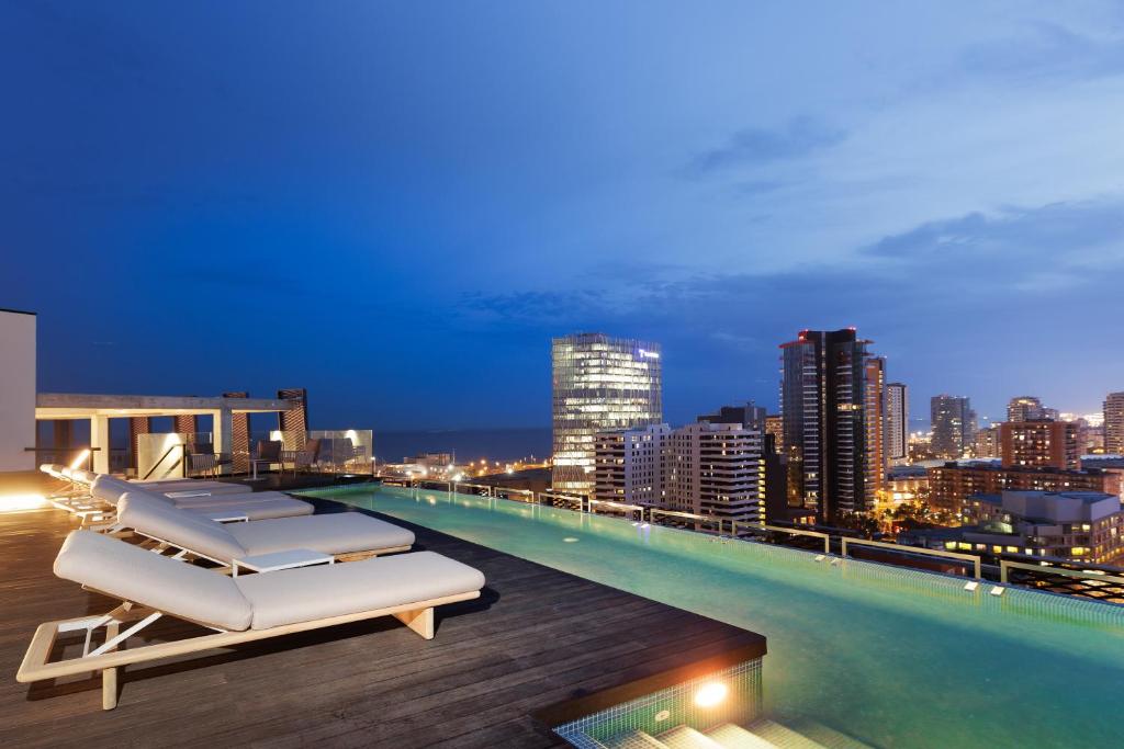 巴塞罗那Tembo Barcelona的一个带躺椅的屋顶游泳池和城市天际线