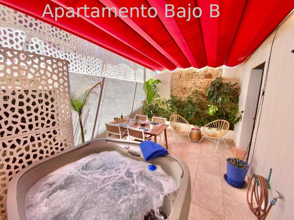 马拉加Apartamentos Simba的阳台的热水浴池,配有红色遮阳伞