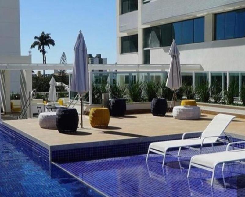 坎普斯戈伊塔卡济斯APART HOTEL AMÉRICA的一座大楼内的游泳池,配有两把椅子和遮阳伞