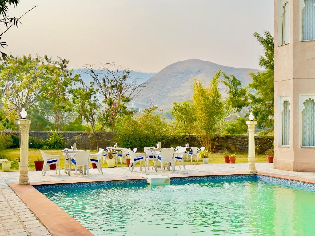 乌代浦Jag Aravali Resort Udaipur- Experience Nature away from city Hustle的一个带桌椅的游泳池和一个游泳池