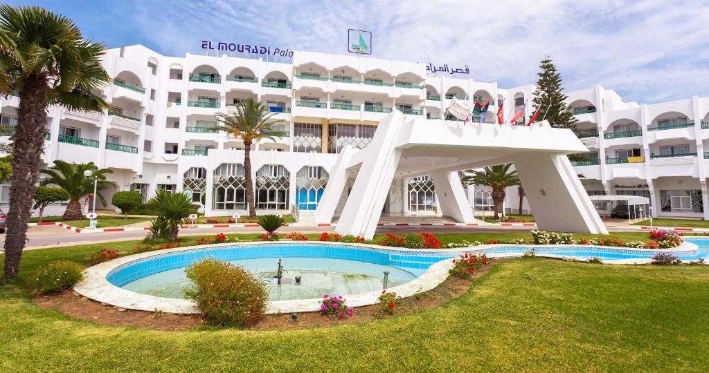 甘达坞伊港El Mouradi Palace的一座白色的大建筑,前面设有一个游泳池