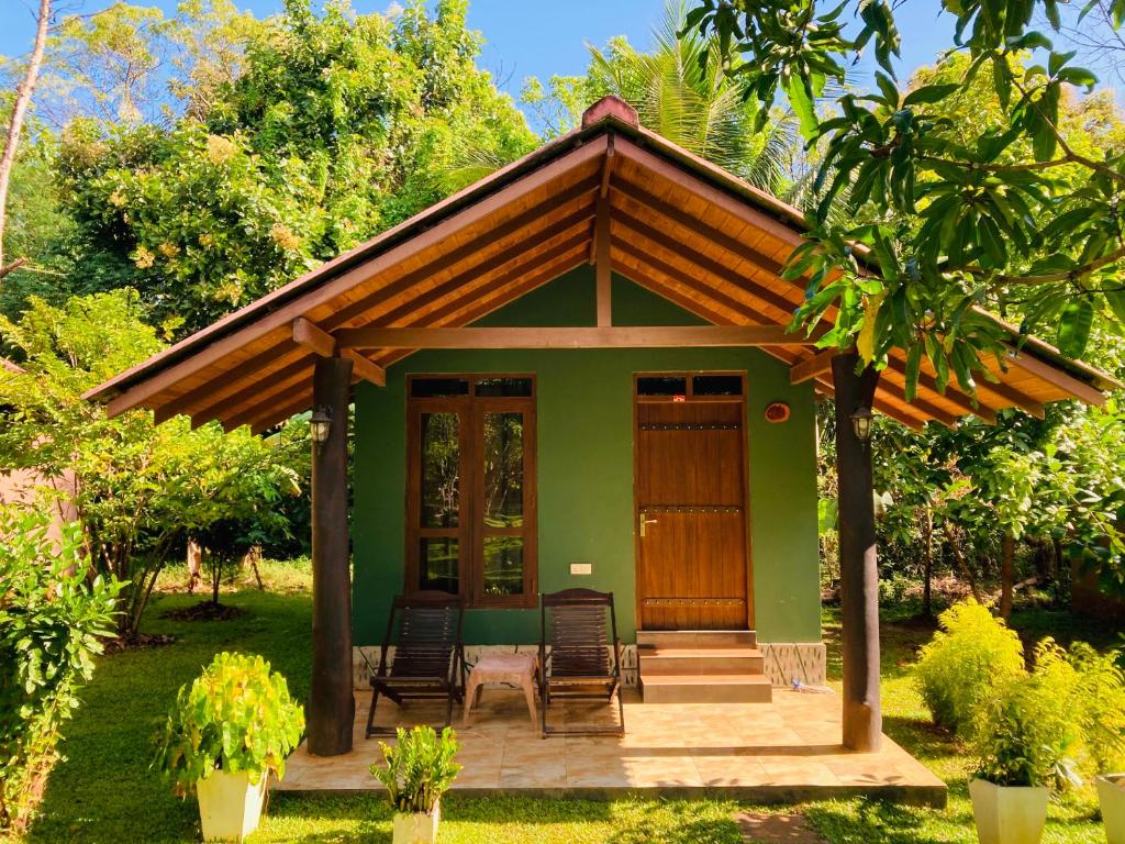 达瓦拉维suncity privacy cottages的一座带椅子和门廊的绿色小房子