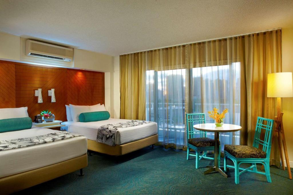 檀香山Oasis Hotel Waikiki的酒店客房带两张床和一张桌子以及椅子。