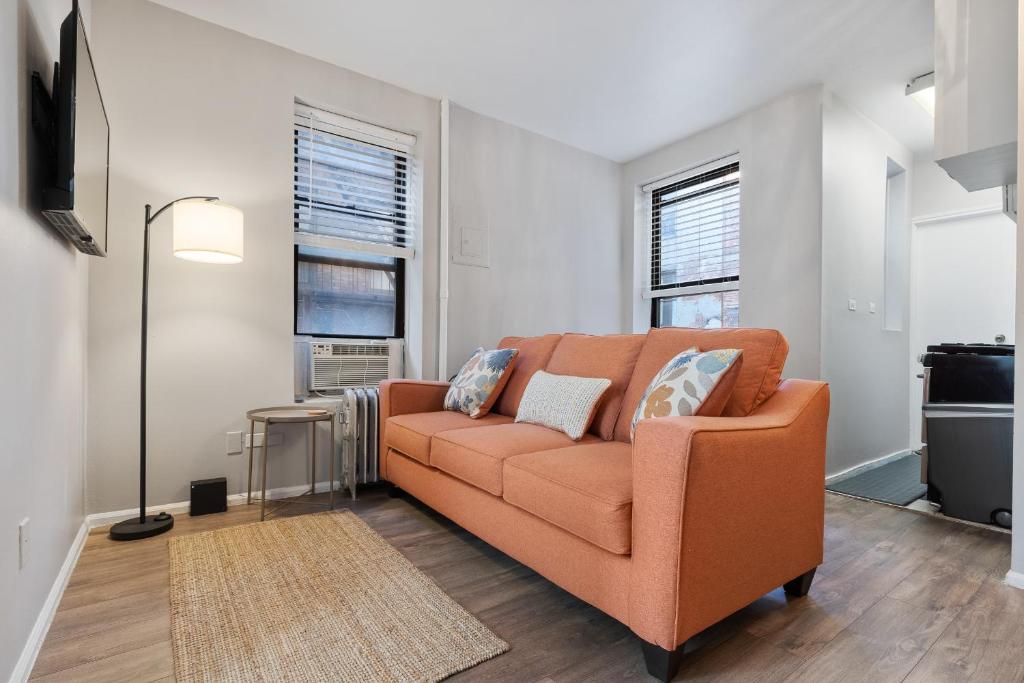 纽约Inspiring Urban Life, Times square Apartments的客厅里设有一张橙色的沙发,设有两扇窗户