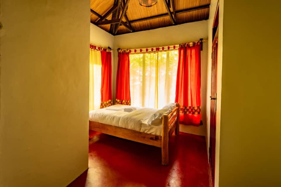 KapchorwaMise cave lodge的一间卧室配有一张带红色窗帘的床和一扇窗户