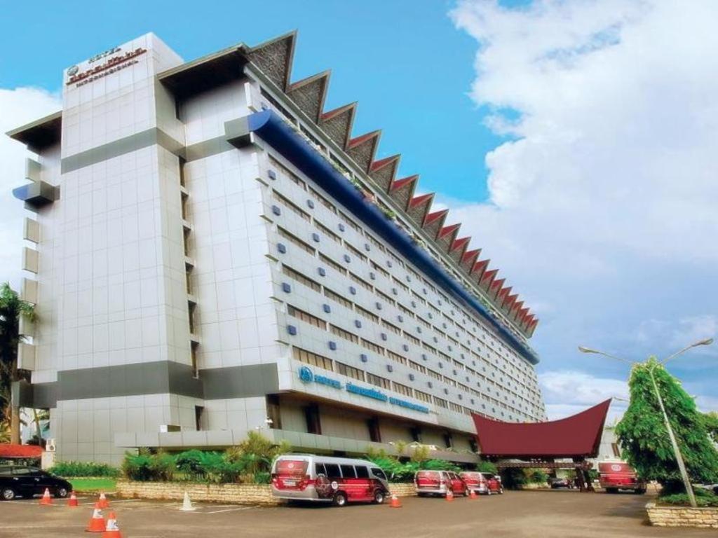 棉兰Danau Toba Hotel International的一座大型建筑,前面有汽车停放