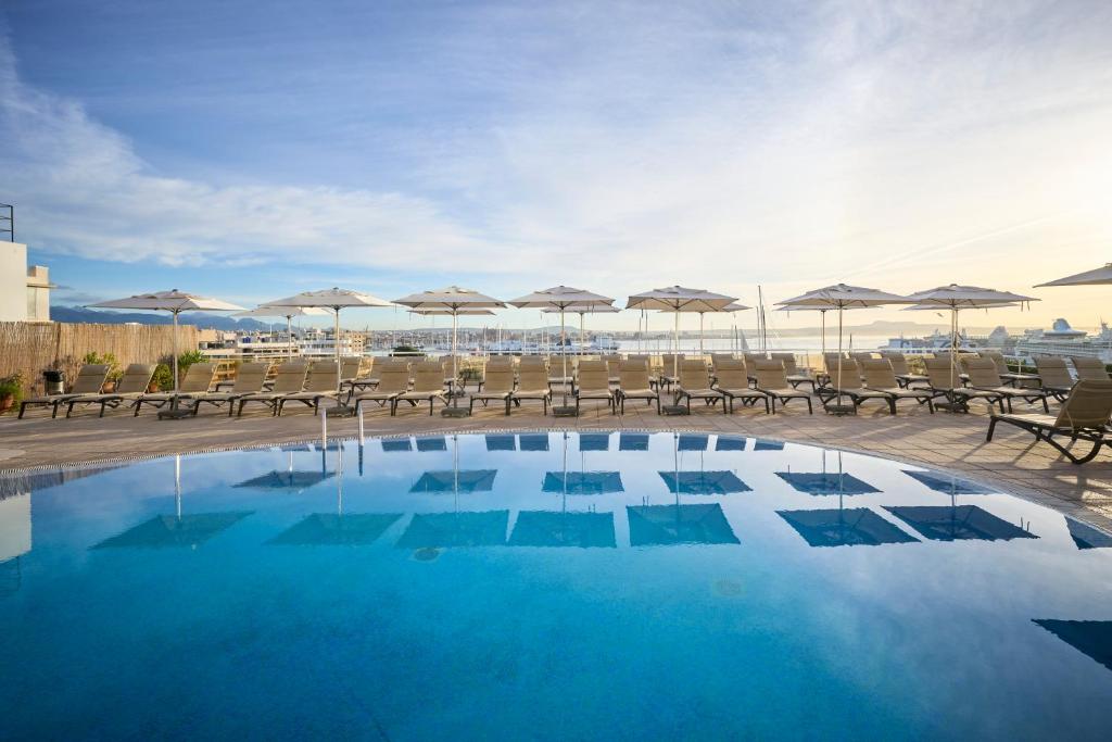 马略卡岛帕尔马加泰罗尼亚马略卡酒店的一座大楼内的游泳池,配有椅子和遮阳伞