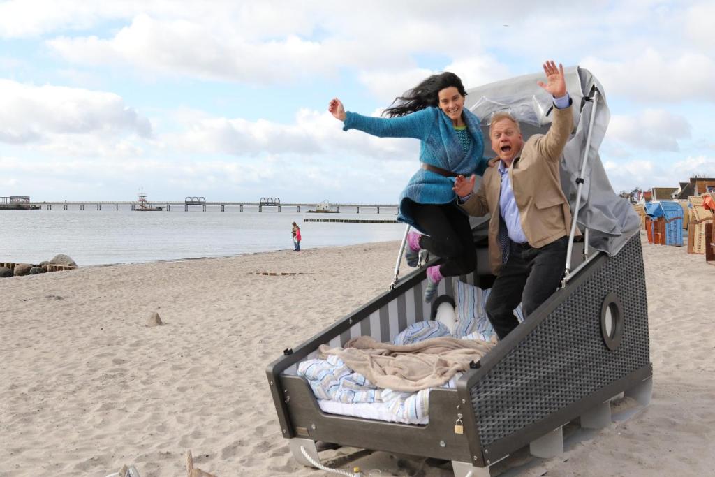克伦胡森Schlafstrandkorb Nr 4的一名男子和一名女子在海滩上跳上拖车