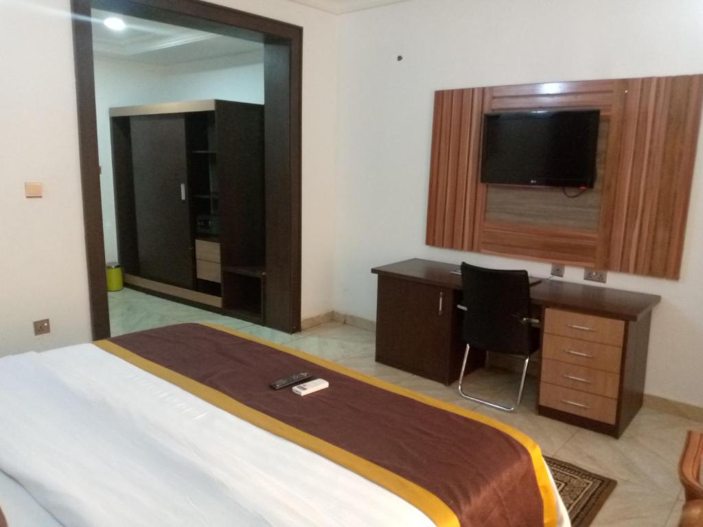 阿布贾Immaculate Diamond Hotel & Apartments的一间卧室配有一张床、一张书桌和一台电视