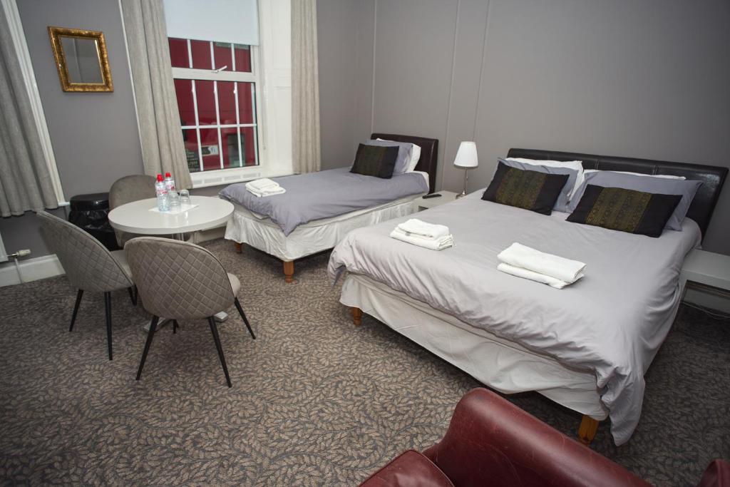 ManorhamiltonFive Glens Inn的酒店客房带两张床和一张桌子以及椅子。