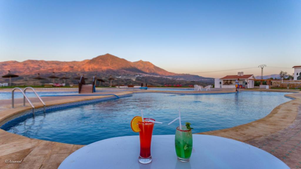 舍夫沙万Hotel El Cortijo & SPA的坐在游泳池旁的桌子上喝两杯饮料
