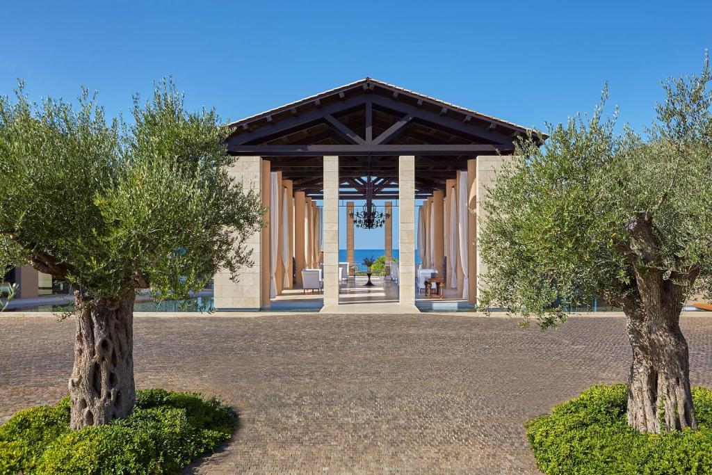 RomanuThe Romanos, a Luxury Collection Resort, Costa Navarino的两棵树在一座带凉亭的建筑前