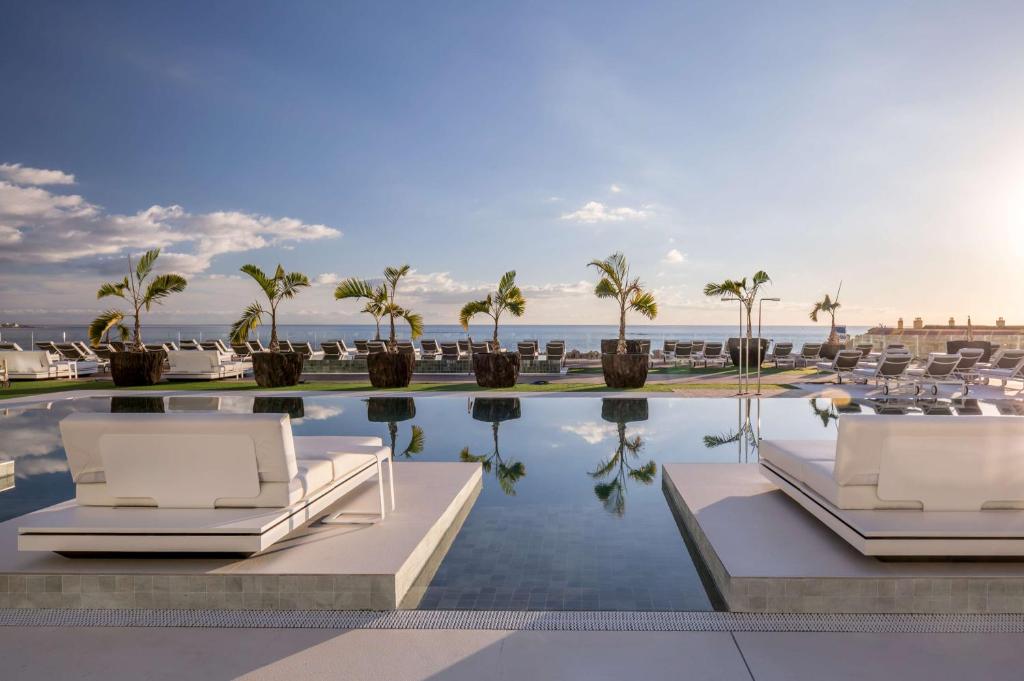 阿德耶Royal Hideaway Corales Suites的一个带椅子和棕榈树的游泳池以及大海
