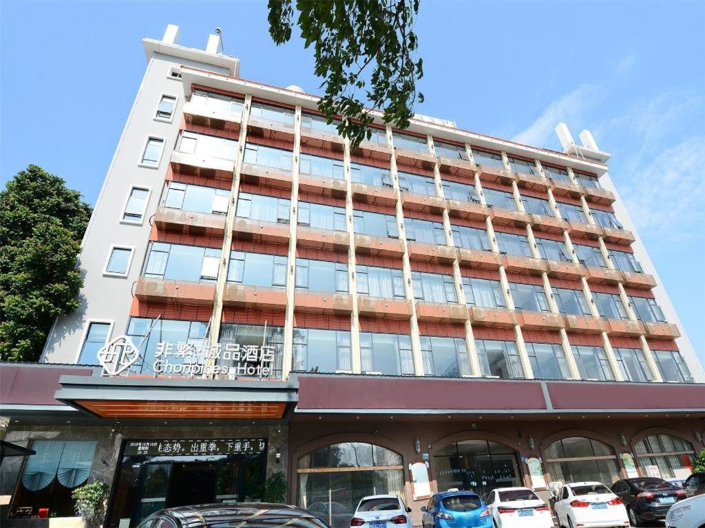 厦门Chonpines Hotel North Xiamen Station Jimei University的一座高大的建筑,前面有汽车停放