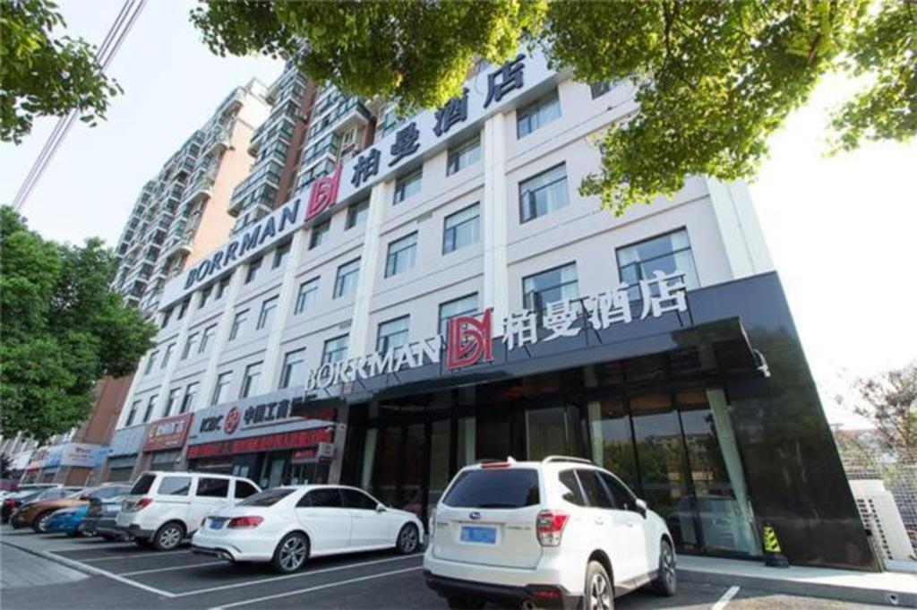 CaoshiBorrman Hotel Jingzhou Jiangjin West Road Wanda Plaza Fantawild的一座白色的大建筑,汽车停在停车场