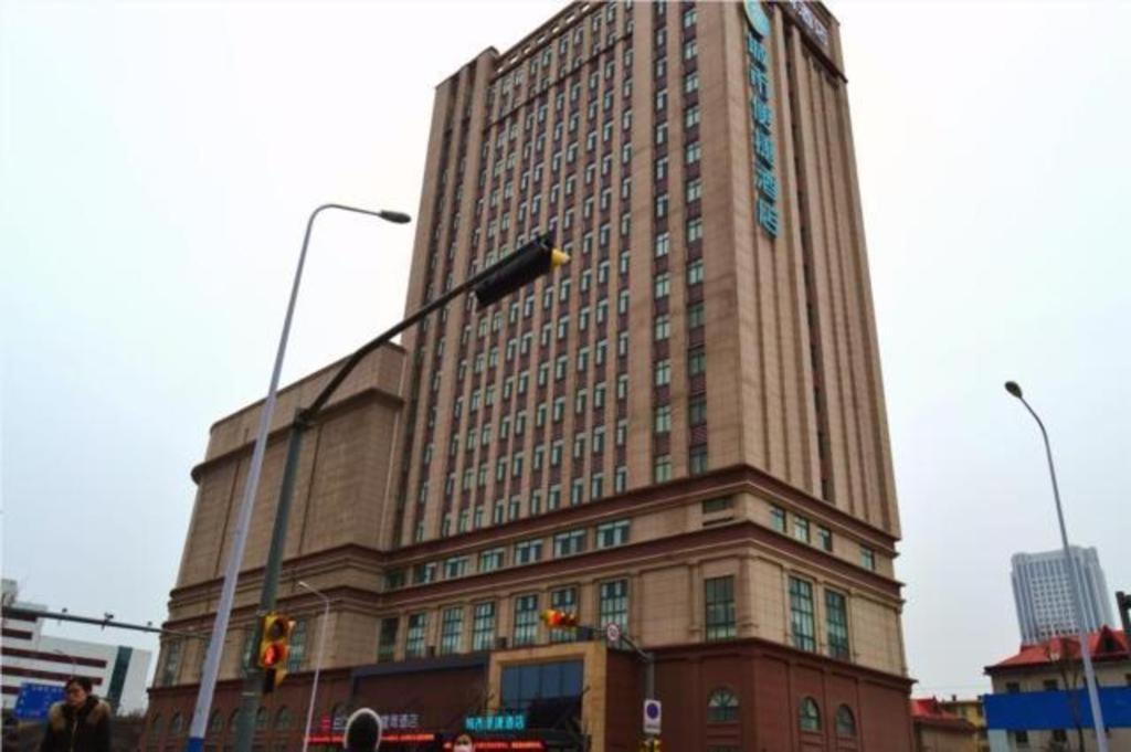 济南City Comfort Inn Jinan Railway Station Daming Lake的城市街道上一座高大的建筑,有交通灯