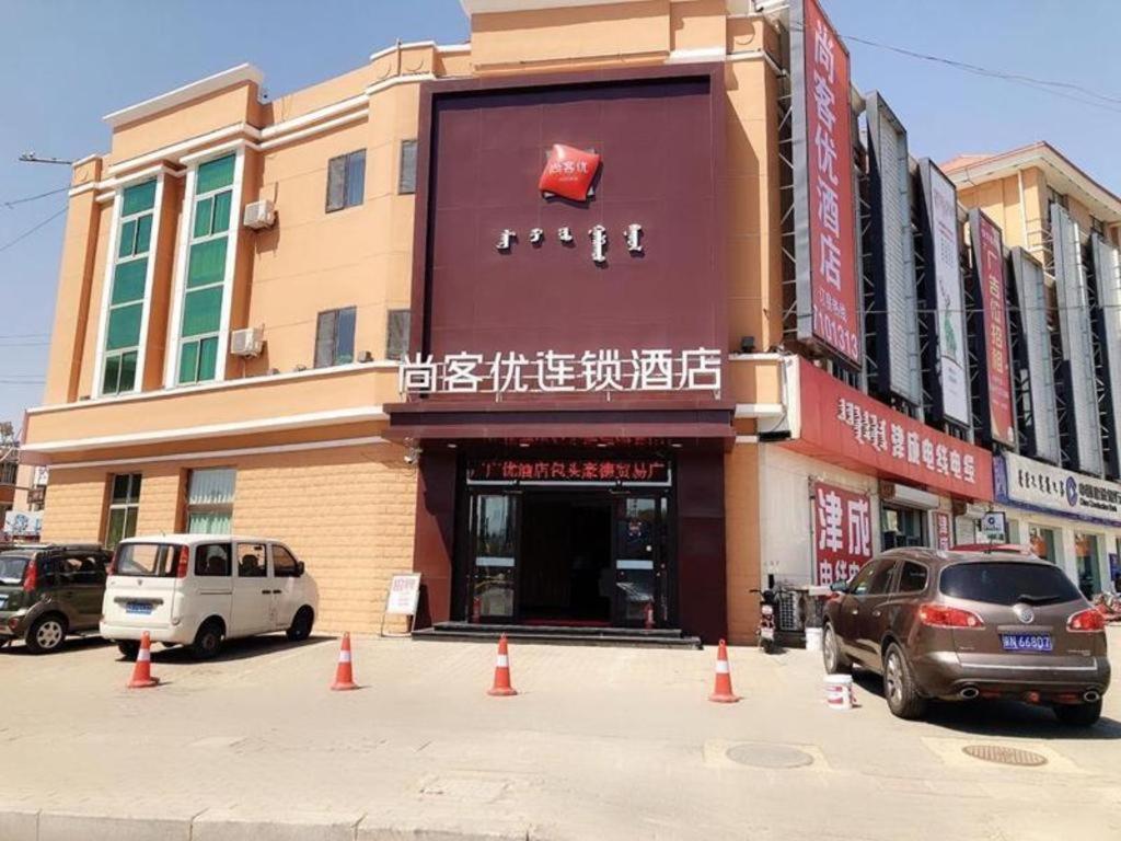 包头Thank Inn Hotel Inner Mongolia Baotou Donghe Haode Trade Plaza的前面有汽车停放的建筑