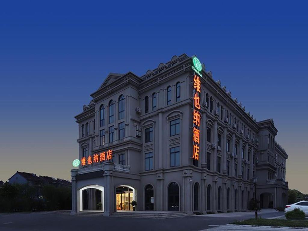 桐乡Vienna Hotel Zhejiang Tongxiang Puyuan的一座大建筑,上面有橙色标志