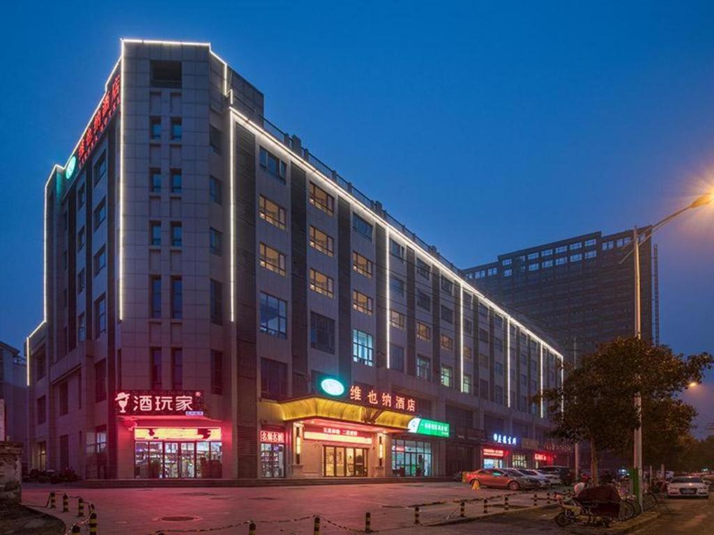 徐州Vienna Hotel Xuzhou Junsheng Plaza Benteng Avenue Metro Station的一座大型建筑,旁边设有 ⁇ 虹灯标志