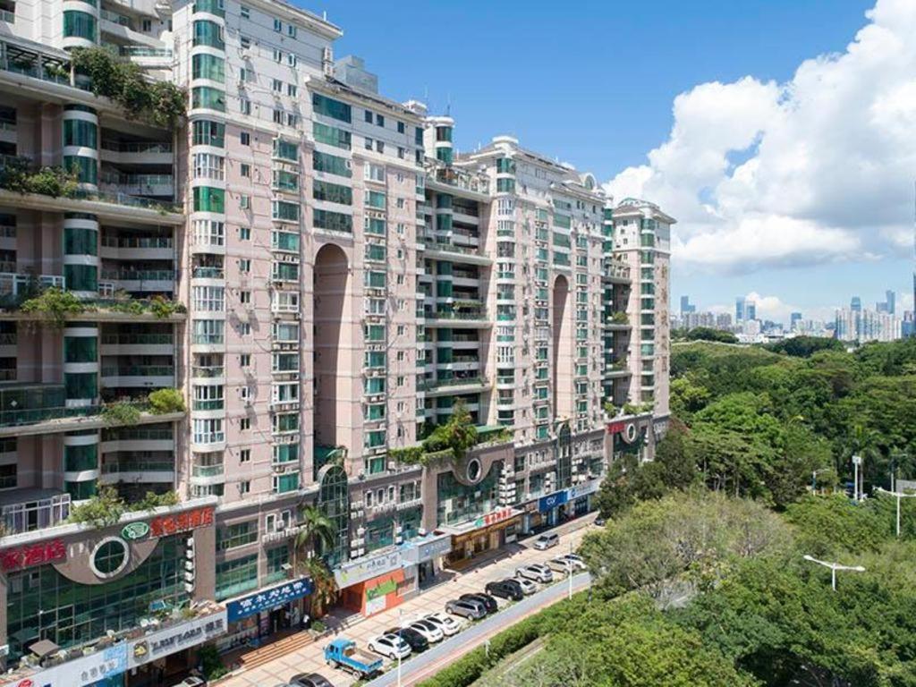 深圳Vienna Hotel Shenzhen Window of the World Qiaochengdong Metro Station的一座大型公寓楼,前面设有停车场