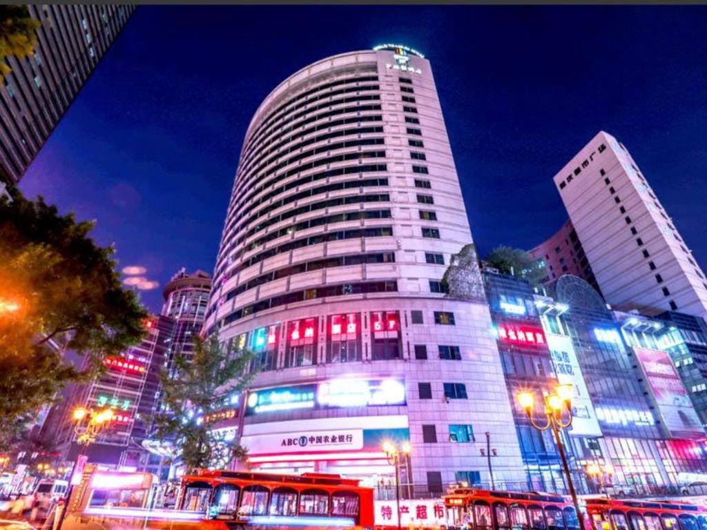 重庆Vienna Hotel Chongqing Jiefangbei Hongyadong的一座高大的建筑,上面有红蓝的灯光