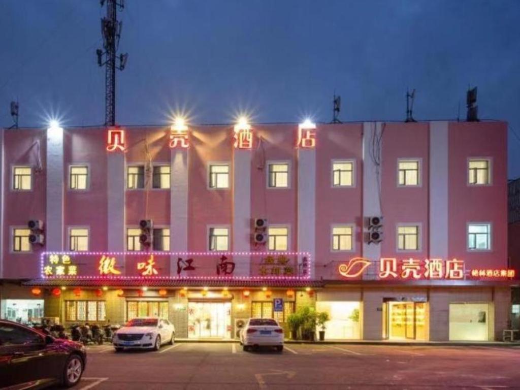 上海Shell Hotel Shnaghai Beiqiao Metro Station的一座大型粉红色建筑,上面有 ⁇ 虹灯标志