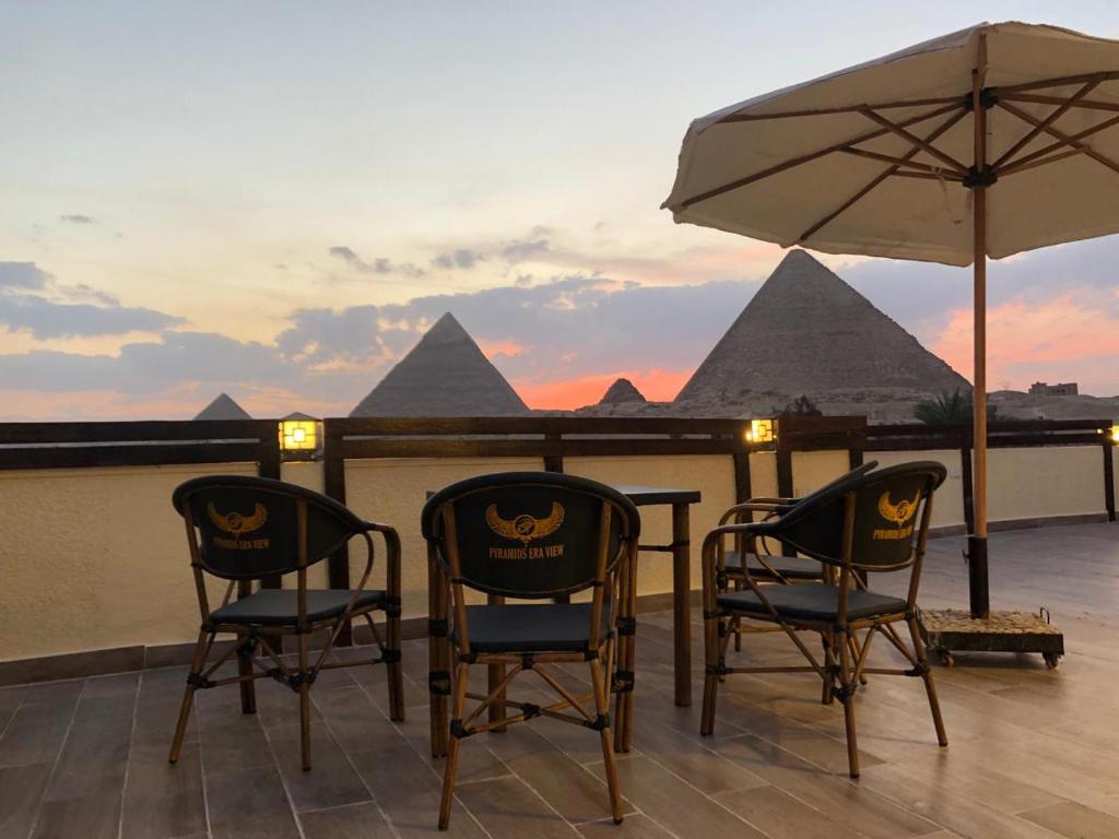 开罗Pyramids Era View的金字塔阳台的两把椅子和一把遮阳伞