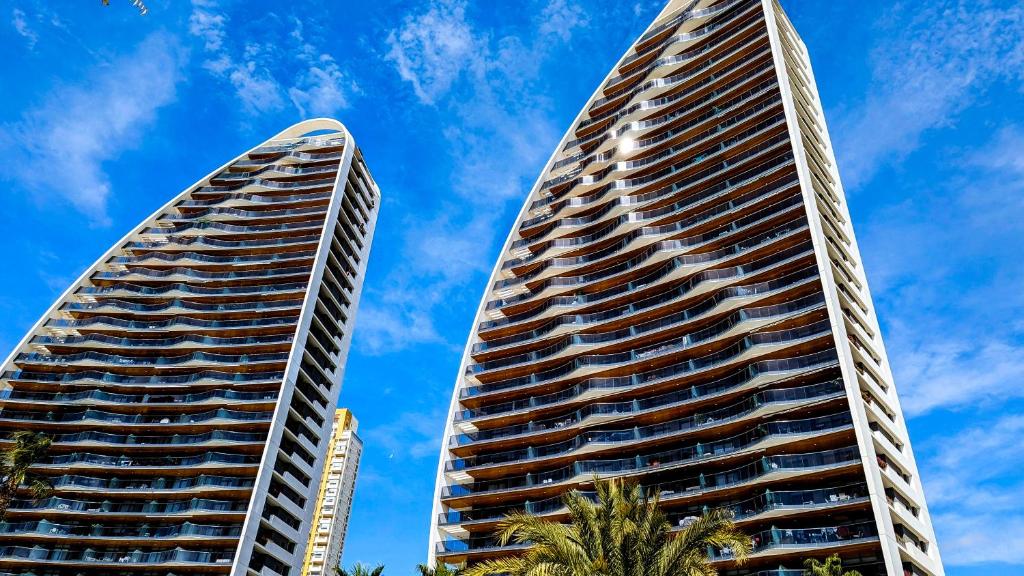 贝尼多姆SUNSET WAVES luxury apartment的两座高大的建筑,棕榈树在蓝天前