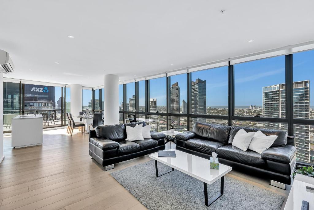 墨尔本Melbourne Lifestyle Apartments – Best Views on Collins的客厅配有黑色皮革家具和大窗户