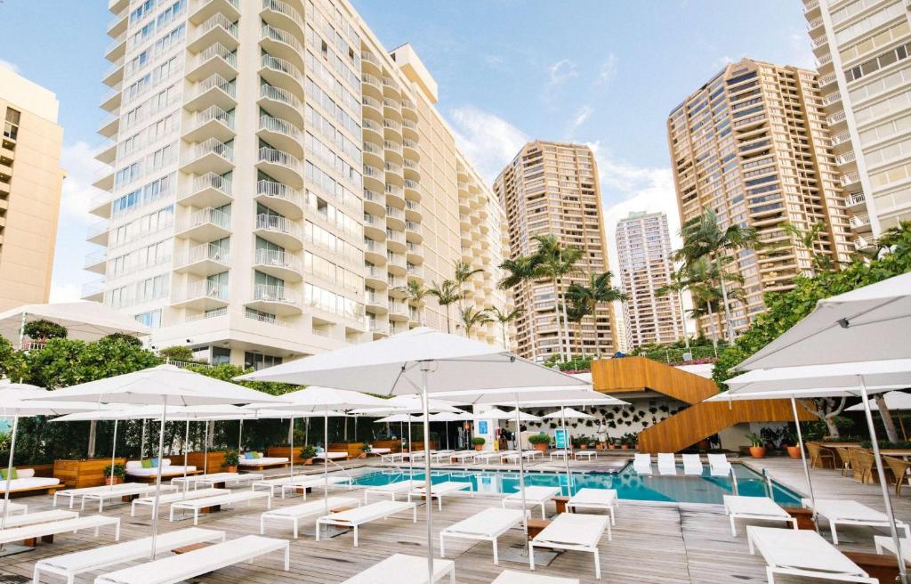檀香山Hilton Vacation Club The Modern Honolulu的一个带白色椅子和遮阳伞的游泳池以及建筑