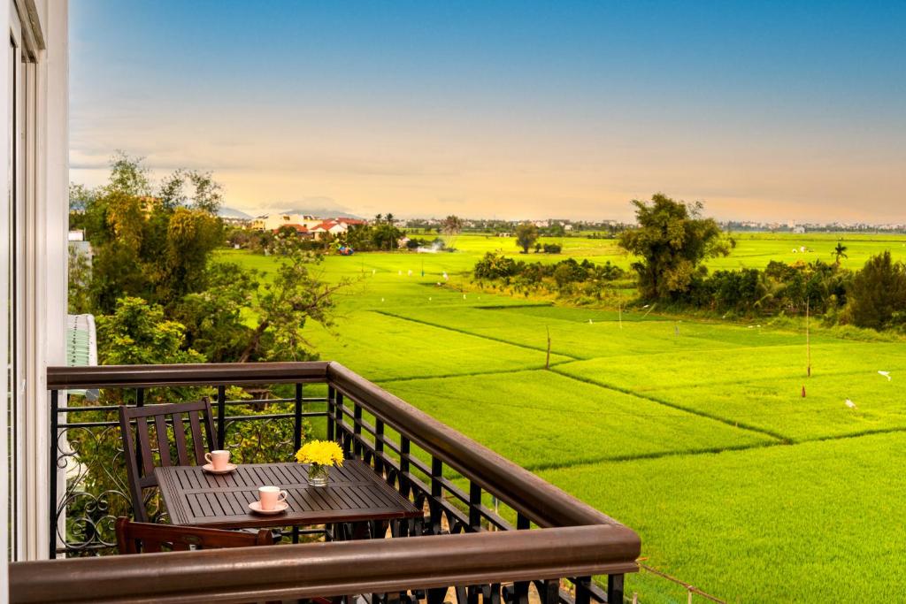 会安Iris De Villa Hoi An的阳台配有桌子,享有绿色田野的景色