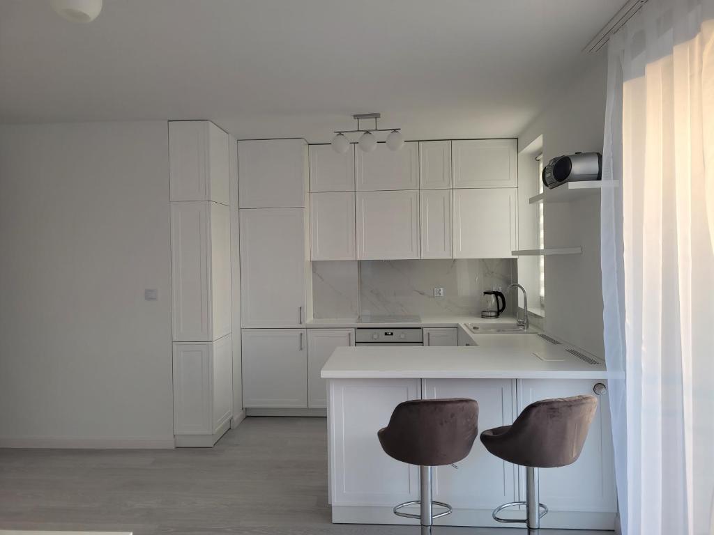 克拉科夫Apartament Mistral的厨房配有白色橱柜和2个酒吧凳